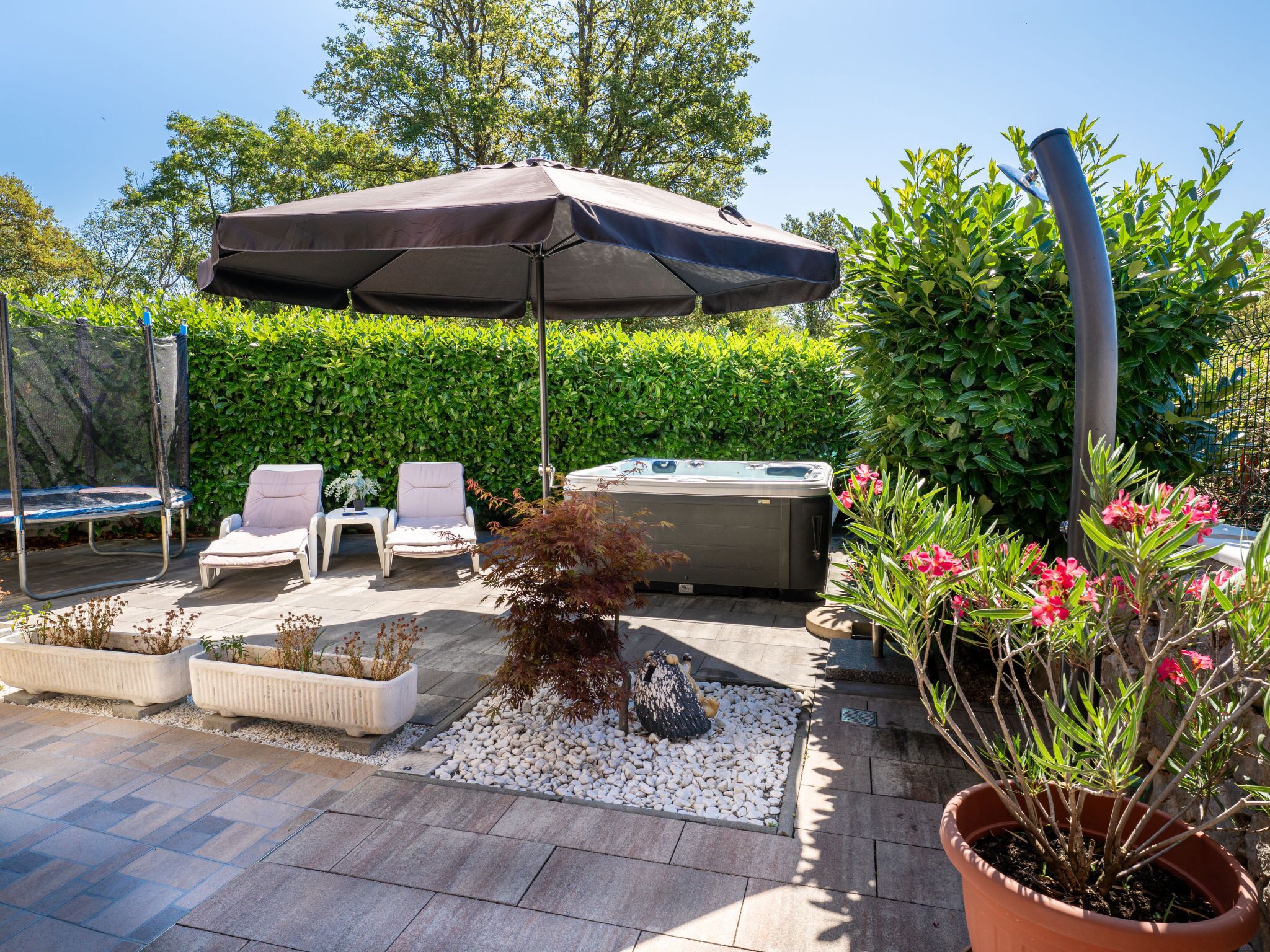 A patio area with a hot tub, lounge chairs, and a large umbrella.