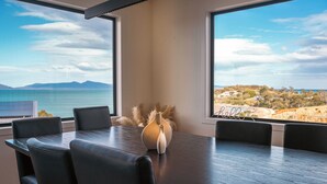 A dining area with a table and chairs, a vase, and a view of the sea and landscape.