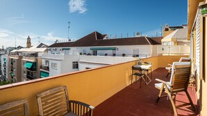 A balcony with wooden chairs and a table, overlooking a cityscape with buildings and a clear sky. - Apartment Goya by Interhome (Estepona)