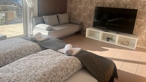 A hotel room with two beds, a sofa, a TV, and a balcony with a city view.
