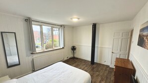 Ein Schlafzimmer mit Bett, Heizkörper, Fenster, Tür und Ventilator.