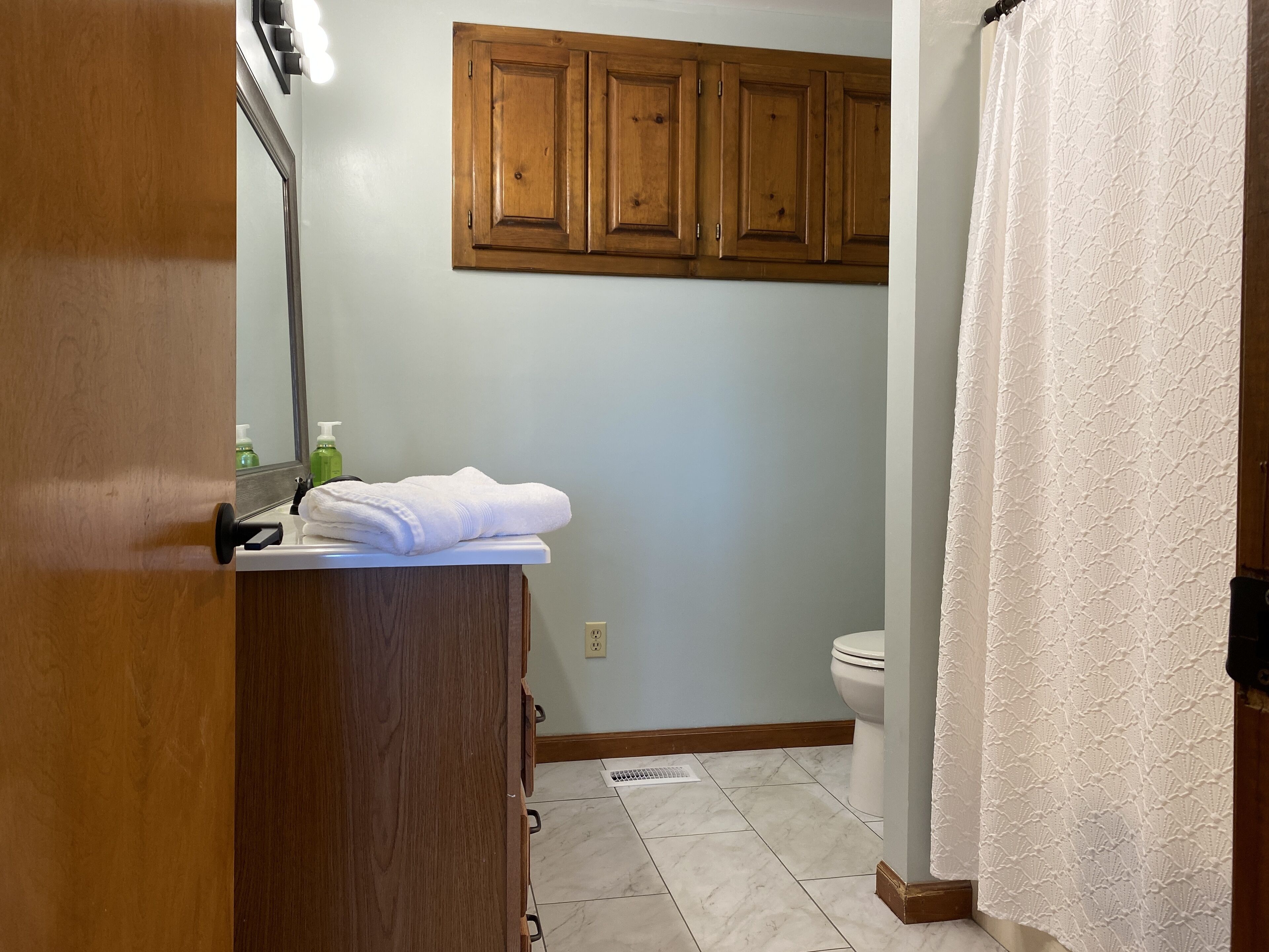 A bathroom with wooden cabinets, a white towel on the counter, a green bottle, and a toilet.