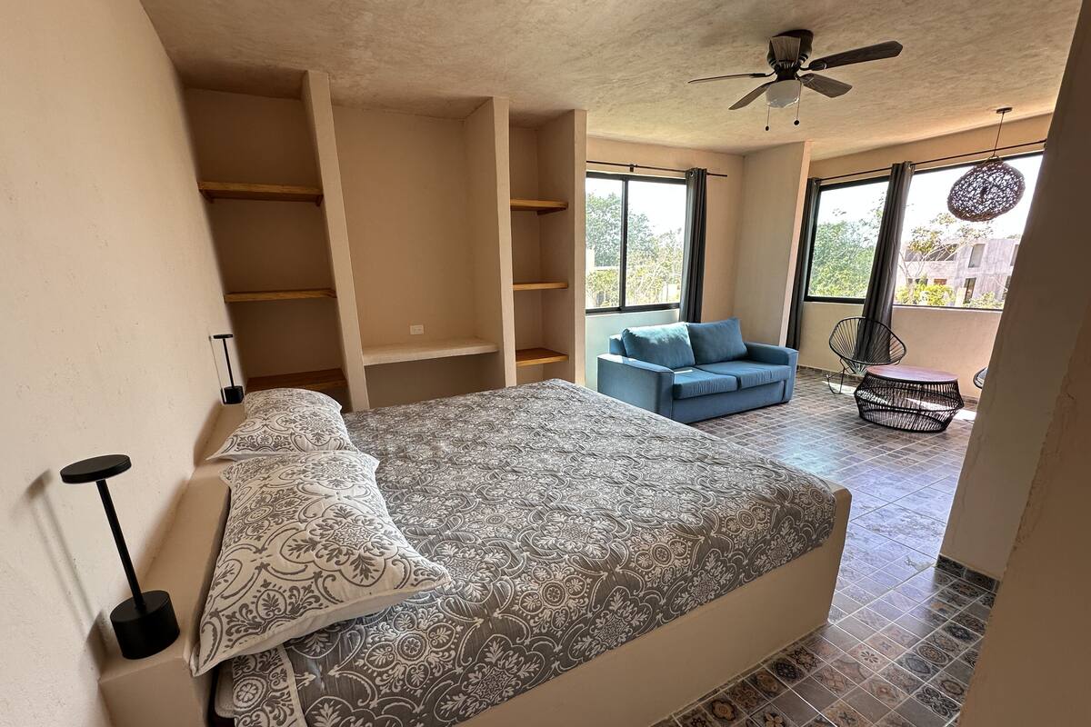 A bedroom with a bed, a blue sofa, and a balcony with a chair.