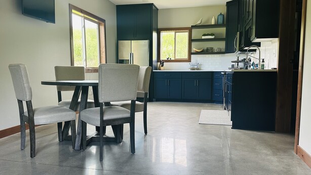 A modern kitchen with dark cabinetry, a stainless steel refrigerator, and a dining area with a table and chairs. - Located in the Heart of MN Lakes Country with much to do in the area. (Lake Park)