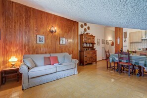 A living room with a wooden wall, a sofa, a dining table with chairs, and a kitchen area. - The Secret Garden in the City center, Bardonecchia, Italy (Bardonecchia)
