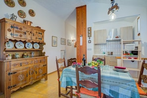 A dining area with a wooden cabinet, a table with a blue tablecloth, chairs, and a kitchen in the background.