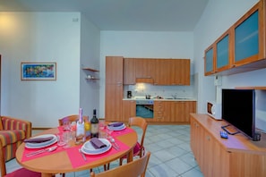 A dining area with a table set for four, a kitchen with wooden cabinets, a microwave, and a television.