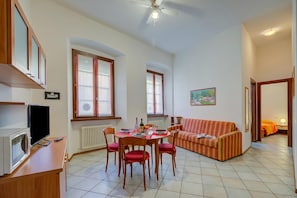 A living room with a dining table, chairs, a sofa, a television, and a ceiling fan.