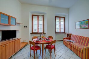 Un salon avec un canapé, un téléviseur, une table à manger avec des chaises et une fenêtre.