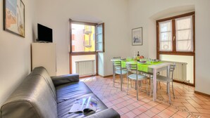 Un salon comprenant un canapé, une table à manger avec des chaises, un téléviseur et une fenêtre donnant sur des immeubles.