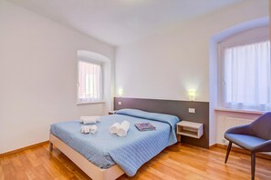 A bedroom with a bed, two bedside tables, a chair, a window, and a radiator.