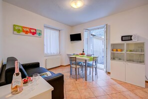 Un salon moderne comprenant un canapé, une table à manger avec des chaises, un téléviseur fixé au mur et un coin cuisine avec un four à micro-ondes et des placards.
