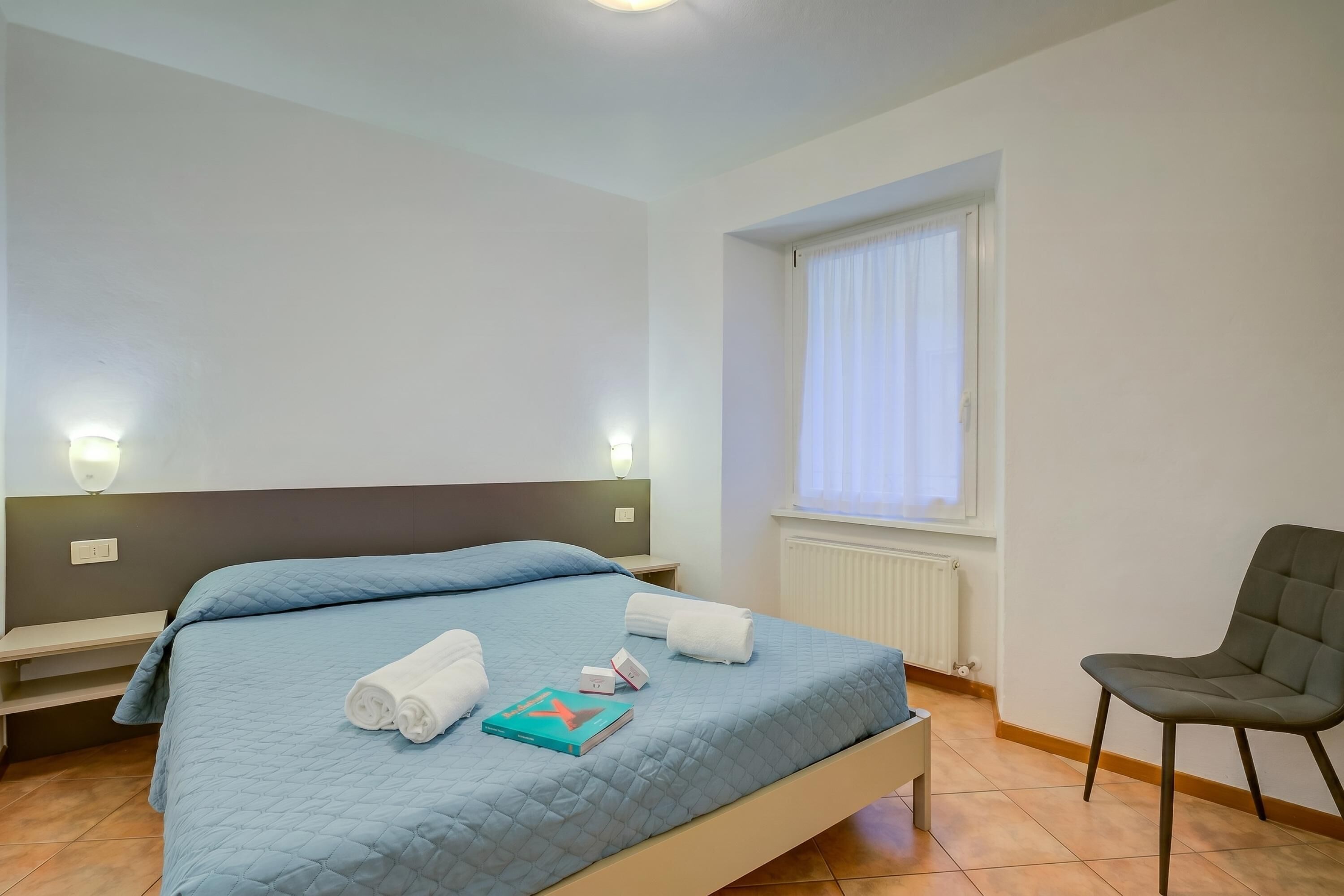 A bedroom with a bed, pillows, a chair, and a window.