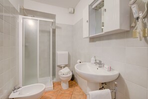 A bathroom with a shower, toilet, bidet, sink, and a hairdryer mounted on the wall.