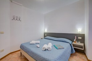 Un lit bien fait, avec une literie bleue, une table de chevet avec une lampe et un luminaire fixé au mur.