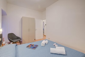 Ett hotellrum med en säng, en stol, en garderob och en dörr som leder till ett annat rum.