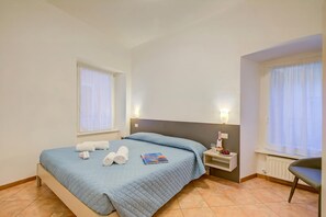 Ein Hotelzimmer mit einem Bett, zwei Nachttischen, einem Sessel und einem Fenster mit Vorhängen.