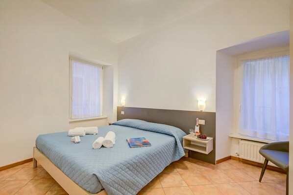 A hotel room with a bed, two bedside tables, a chair, and a window with curtains. - Casa Alpino 2, Riva del Garda, Italy (Riva del Garda)