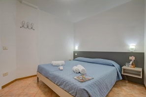 Une chambre d’hôtel comprenant un lit, une table de chevet, une lampe fixée au mur et un porte-serviettes.
