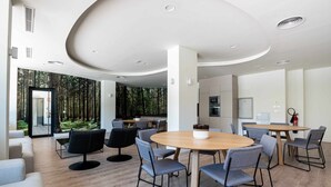 Une salle de conférence moderne, dotée d’une table ronde en bois, de chaises rembourrées de couleur grise et offrant une vue sur la forêt grâce à de grandes fenêtres.
