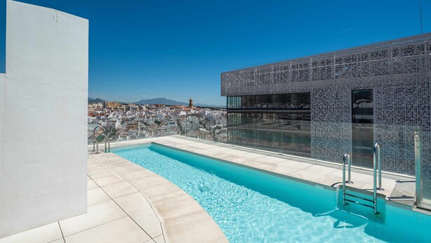 Une piscine sur le toit offrant une vue dégagée sur le paysage urbain et un bâtiment moderne doté d’une façade à motifs.