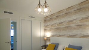 Une chambre à coucher comprenant un lit, une table de chevet, une lampe fixée au mur et une porte donnant sur une autre pièce.