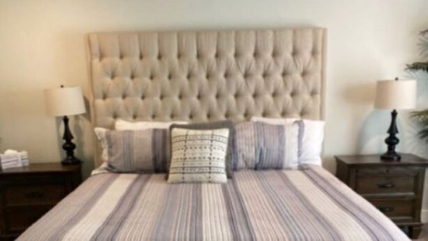 A bedroom with a tufted headboard, a striped bedspread, two bedside tables with lamps, and a nightstand with a lamp.