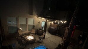 A hot tub with blue lighting, surrounded by outdoor seating and a fire pit.