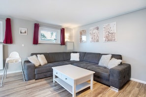 Una sala moderna con un sofá seccional gris, una mesa de centro blanca y una silla blanca.
