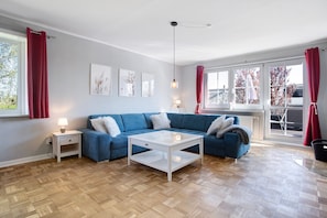 Un salón moderno con un sofá seccional azul, una mesa de centro blanca y un piso de madera con diseño de espiga.