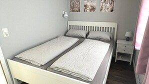 Una cama individual con cabecera blanca, una mesita de noche con lámpara y tres cuadros enmarcados en la pared.