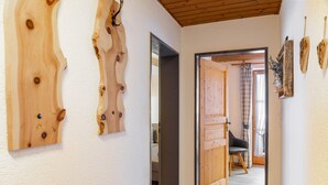 A hallway with wooden wall art, a wooden door, and a view into a room with a chair and curtains. - Apartment Reintal with Mountain View, Balcony, and Wi-Fi (Grainau)