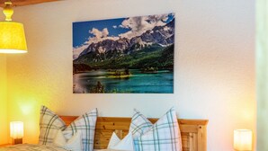 A bedroom with a bed, two bedside lamps, a wooden headboard, and a wall-mounted picture of a mountain landscape. - Apartment Reintal with Mountain View, Balcony, and Wi-Fi (Grainau)