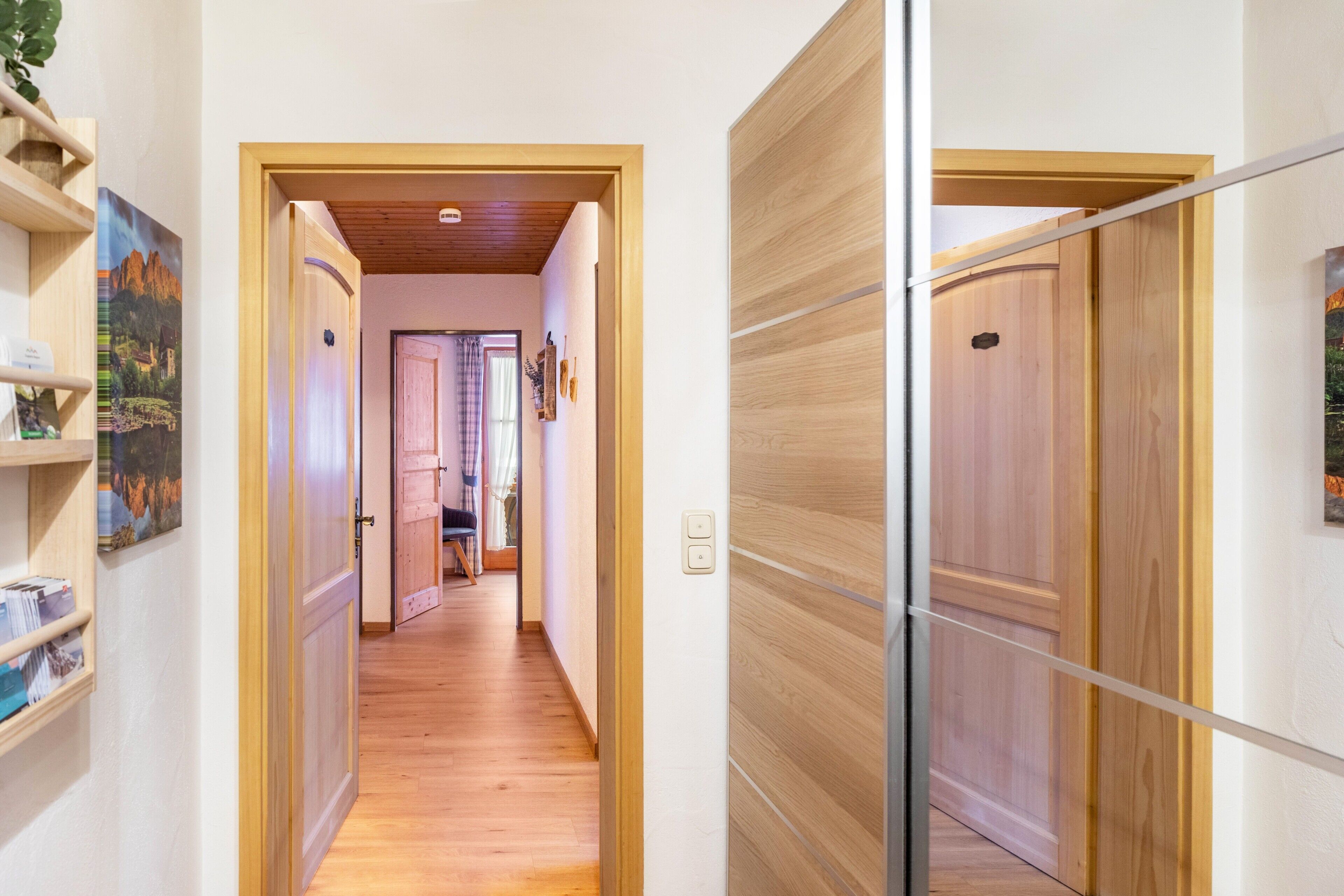 A hallway with wooden flooring, a door with a glass panel, and a shelf with books and a framed picture.