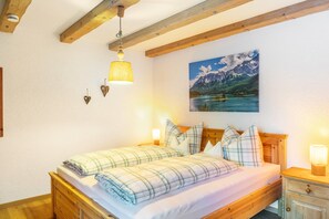 A bedroom with a wooden bed, two bedside lamps, a painting of a mountain landscape, and a wooden ceiling. - Apartment Reintal with Mountain View, Balcony, and Wi-Fi (Grainau)