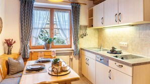 A cozy kitchen with wooden cabinets, a dining table set for two, and a window with curtains. - Apartment Reintal with Mountain View, Balcony, and Wi-Fi (Grainau)
