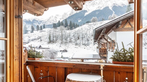 A wooden balcony with a table and chairs, overlooking a snowy mountain landscape. - Apartment Reintal with Mountain View, Balcony, and Wi-Fi (Grainau)