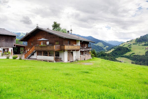 Un chalet en bois doté d’un balcon, situé dans une vallée verdoyante, avec des montagnes en toile de fond.