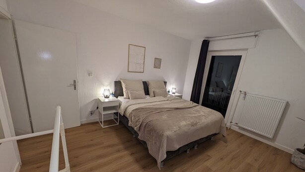Une chambre à coucher avec un lit, des tables de chevet, un radiateur et une fenêtre avec des rideaux.