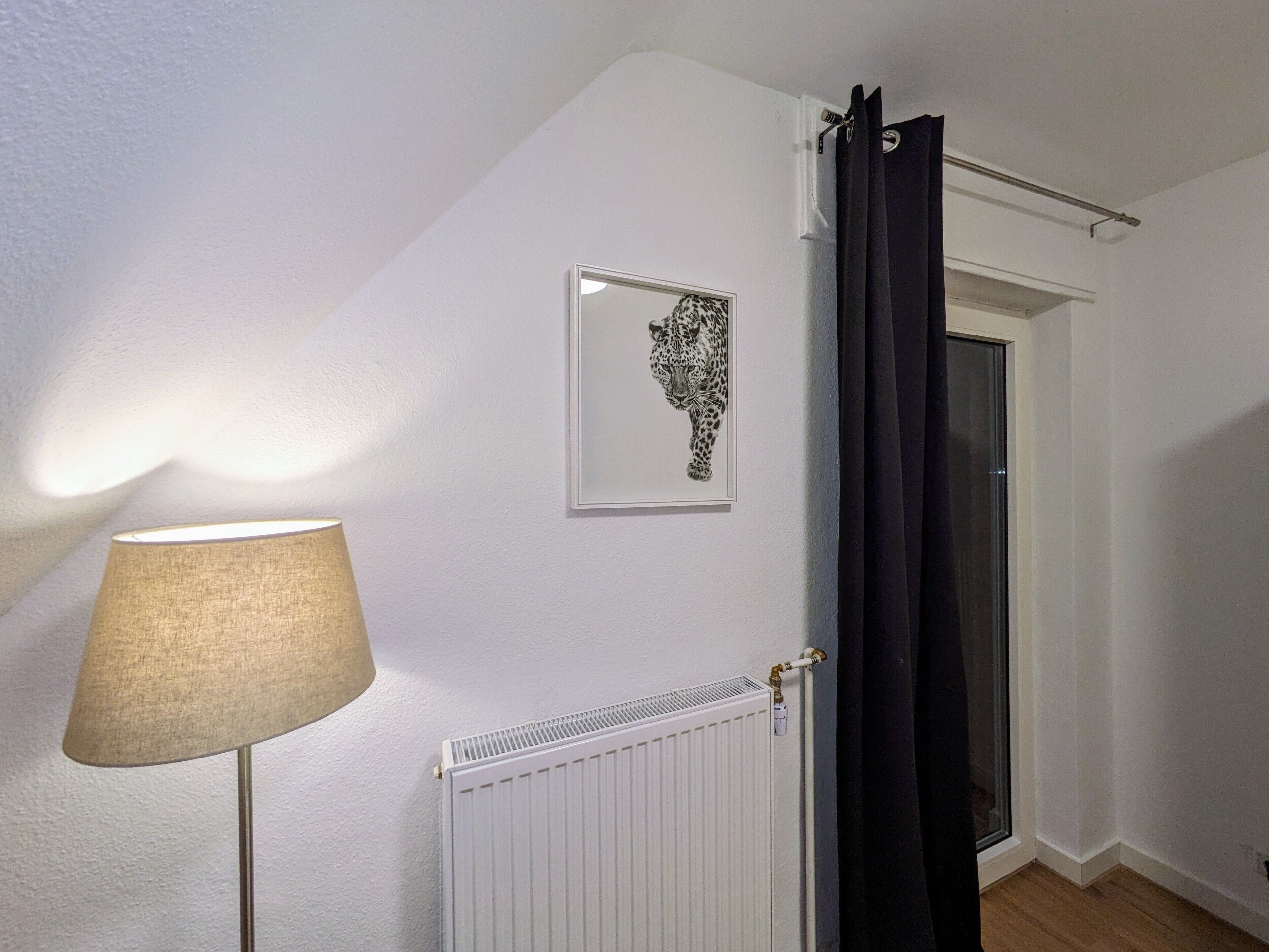 Ein Zimmer mit Heizkörper, einem gerahmten Bild eines Leoparden, einem schwarzen Vorhang und einer Lampe.