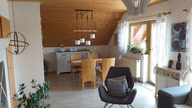 Ein gemütlicher Loft-Raum mit Essbereich, einem schwarzen Stuhl mit Sitzkissen, Holzboden und einer Pendelleuchte.