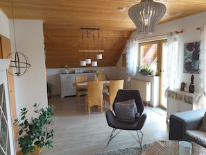 A cozy loft-style room with a dining area, a black chair with a cushion, a wooden ceiling, and a hanging light fixture.