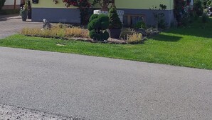Ein zweistöckiges Haus mit geneigtem Dach, einer Veranda mit Holzgeländer und einem Garten mit verschiedenen Pflanzen und Blumen.