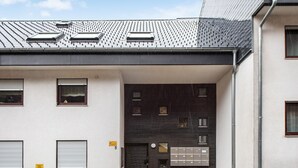 Un bâtiment moderne à la façade sombre, doté de nombreuses fenêtres et d’une fente à lettres bien visible.