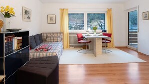 Un salon comprenant un canapé, une table à manger avec des chaises, un radiateur et une fenêtre avec des rideaux.