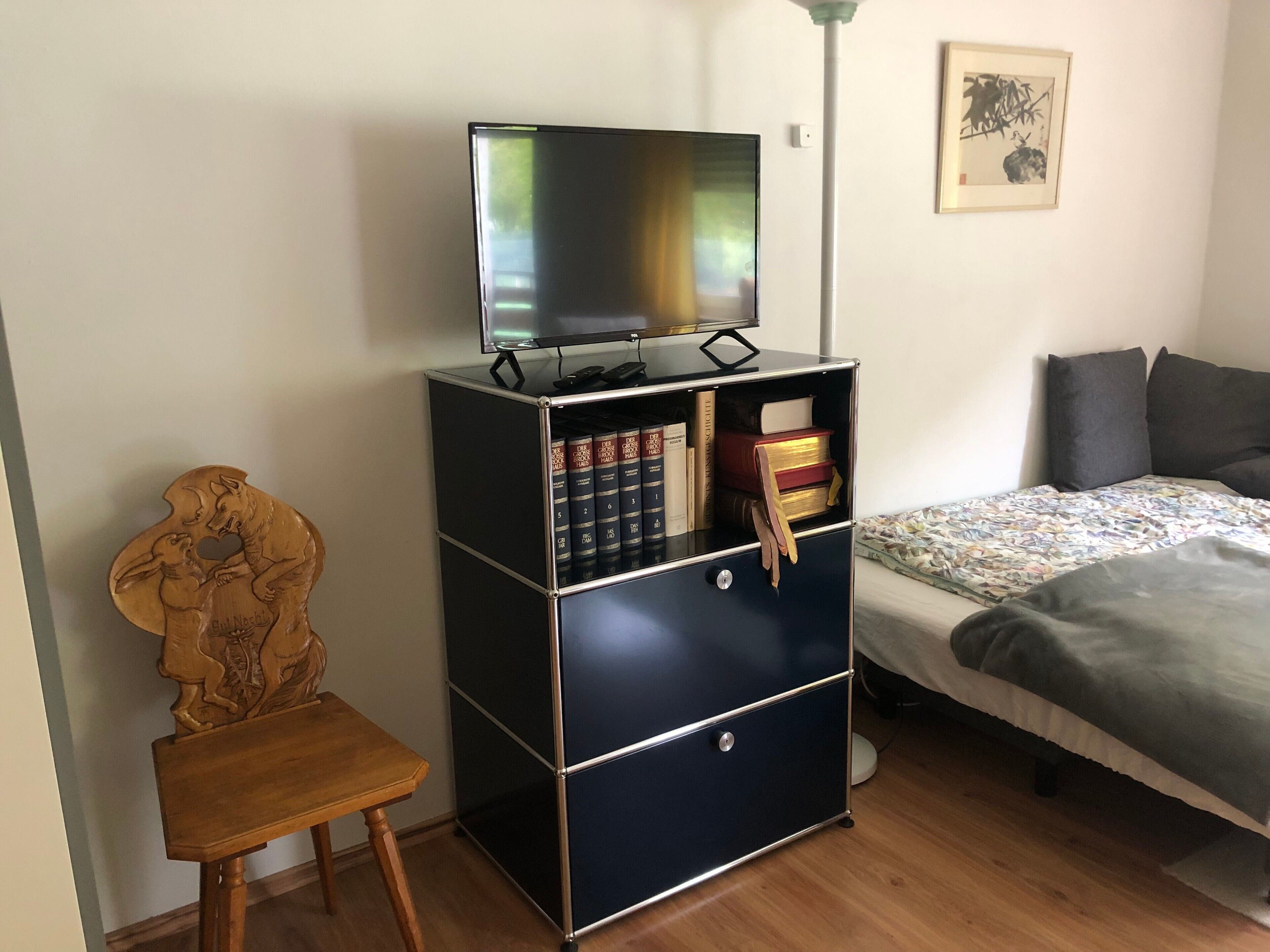 Et værelse med en seng, et skrivebord med tv, en bogreol og en træstol.