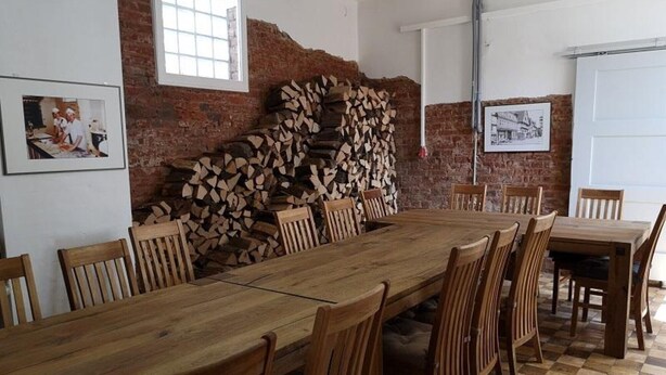 Une longue table en bois, entourée de chaises, un mur en briques et une cheminée avec une pile de bûches.