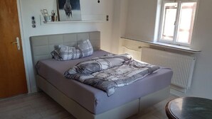Et soveværelse med seng, natbord, vindue og radiator.