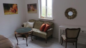 Et værelse med en sofa, et rundt bord, en stol, et vindue og to billeder hængt på væggen.