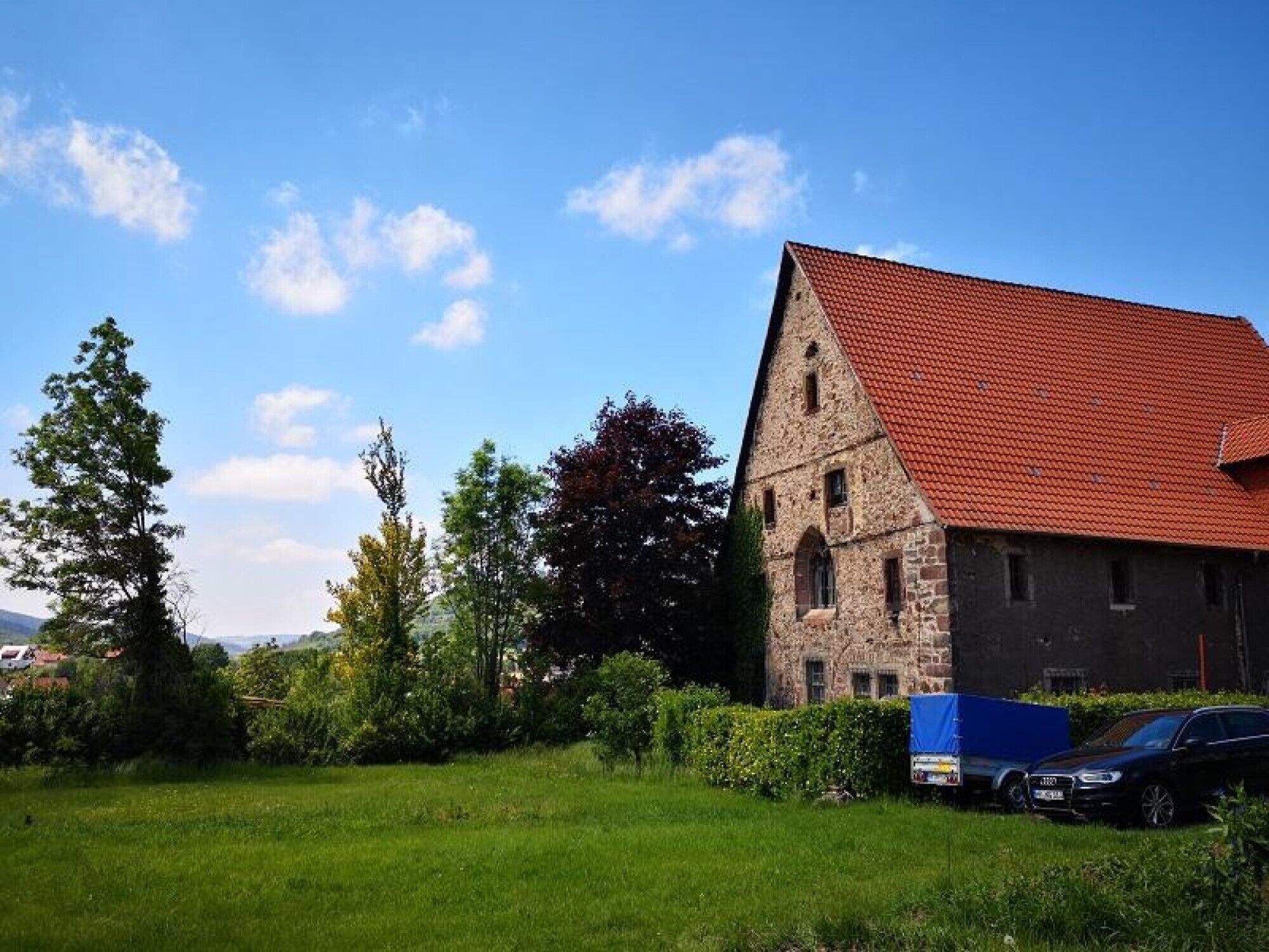 Un bâtiment en pierre avec un toit rouge, entouré de verdure et sous un ciel dégagé.
